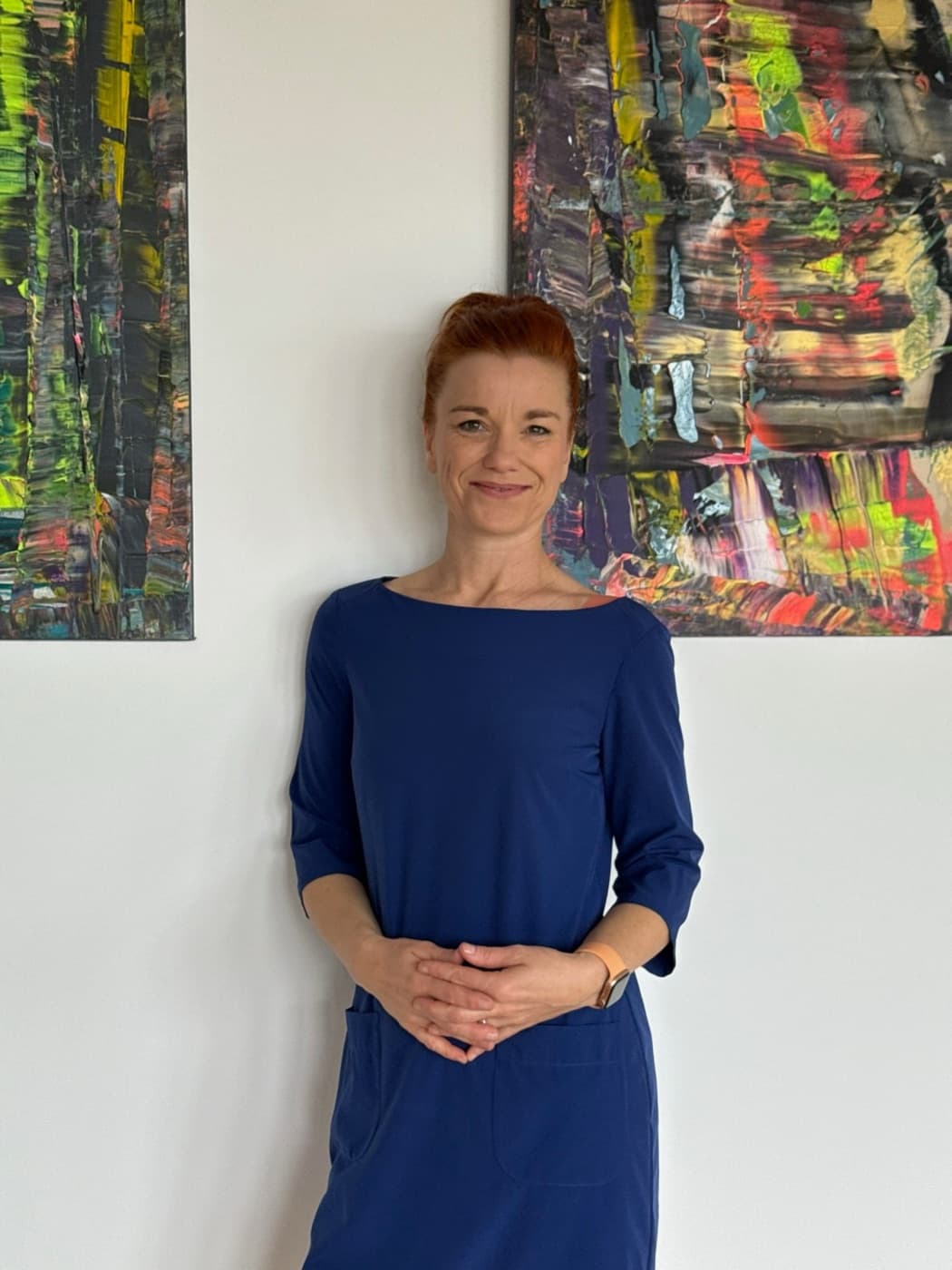 Christiane Schmieder im blauen Kleid vor zwei farbigen abstrakten Gemälden
